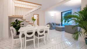 A modern living room with a dining area, a staircase, and a large window. - Jacaranda House - My Rental Homes (Sant'Agnello)