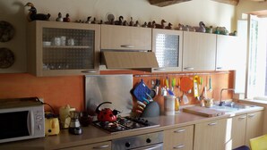 A kitchen with wooden cabinets, a microwave, a stove, and various utensils hanging on the wall. - Casa O is a 19th-century, restored, stone house with garden IT046022C2LZ5R4HQX (Pescaglia.)