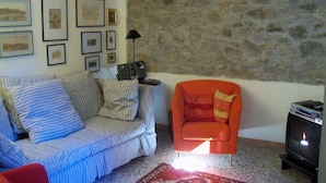A living room with a striped sofa, an orange armchair, a stone wall, and framed pictures on the wall. - Casa O is a 19th-century, restored, stone house with garden IT046022C2LZ5R4HQX (Pescaglia.)