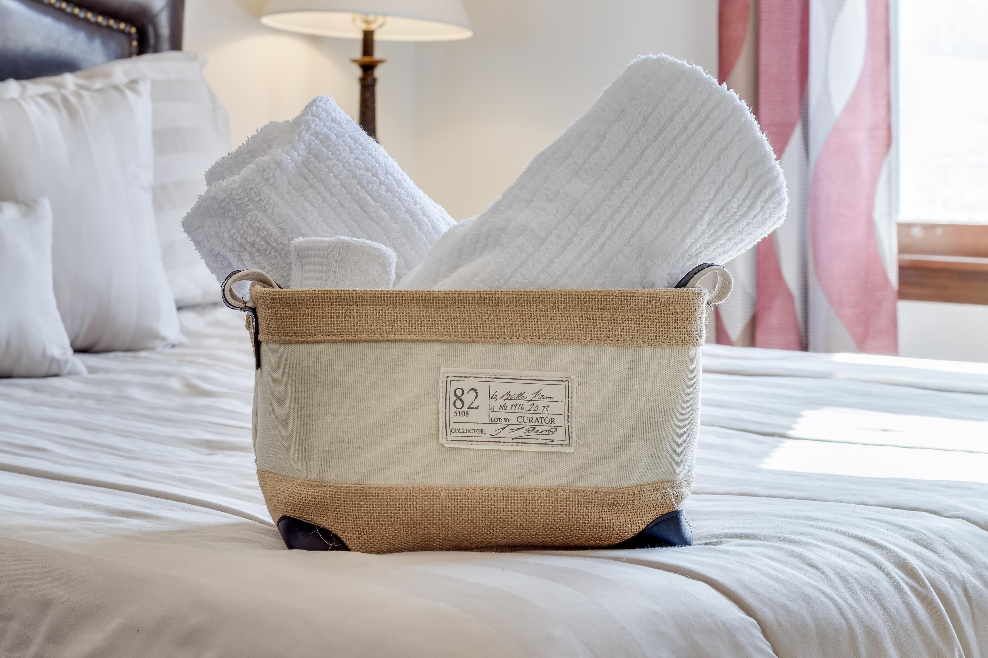 Una cesta de mimbre llena de toallas blancas sobre una cama.