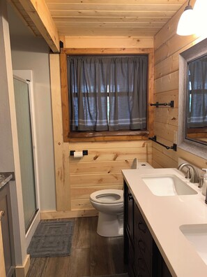 Een kleine houten badkamer met toilet, wastafel en raam met gordijnen.