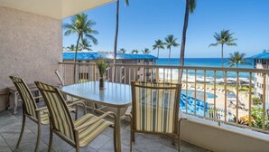 Ein Balkon mit Blick auf Strand und Pool, ausgestattet mit gestreiften Stühlen und einem Tisch.