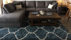 Ein Wohnzimmer mit einem Ecksofa, einem Couchtisch und einem gemusterten Teppich.