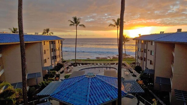 Ein Hotel mit Pool, Palmen und Blick auf den Ozean bei Sonnenuntergang.