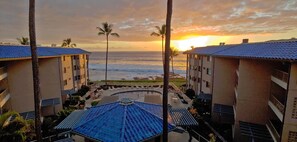 Een hotel met een zwembad, palmbomen en uitzicht op de oceaan bij zonsondergang.