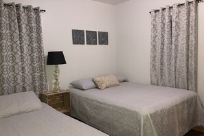 A bedroom with two beds, a nightstand with a lamp, and three wall art pieces.