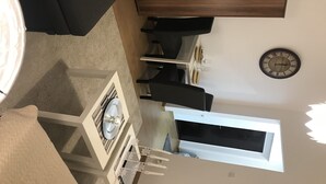 Ein modernes Wohnzimmer mit einem dunklen Sofa, einem Esstisch mit Stühlen, einer Uhr an der Wand und einem Fenster.
