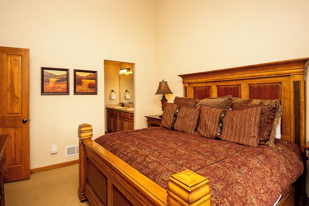 A bedroom with a large bed, wooden headboard, and a nightstand with a lamp.