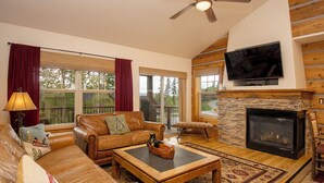 A cozy living room with leather sofas, a fireplace, a television, and large windows.