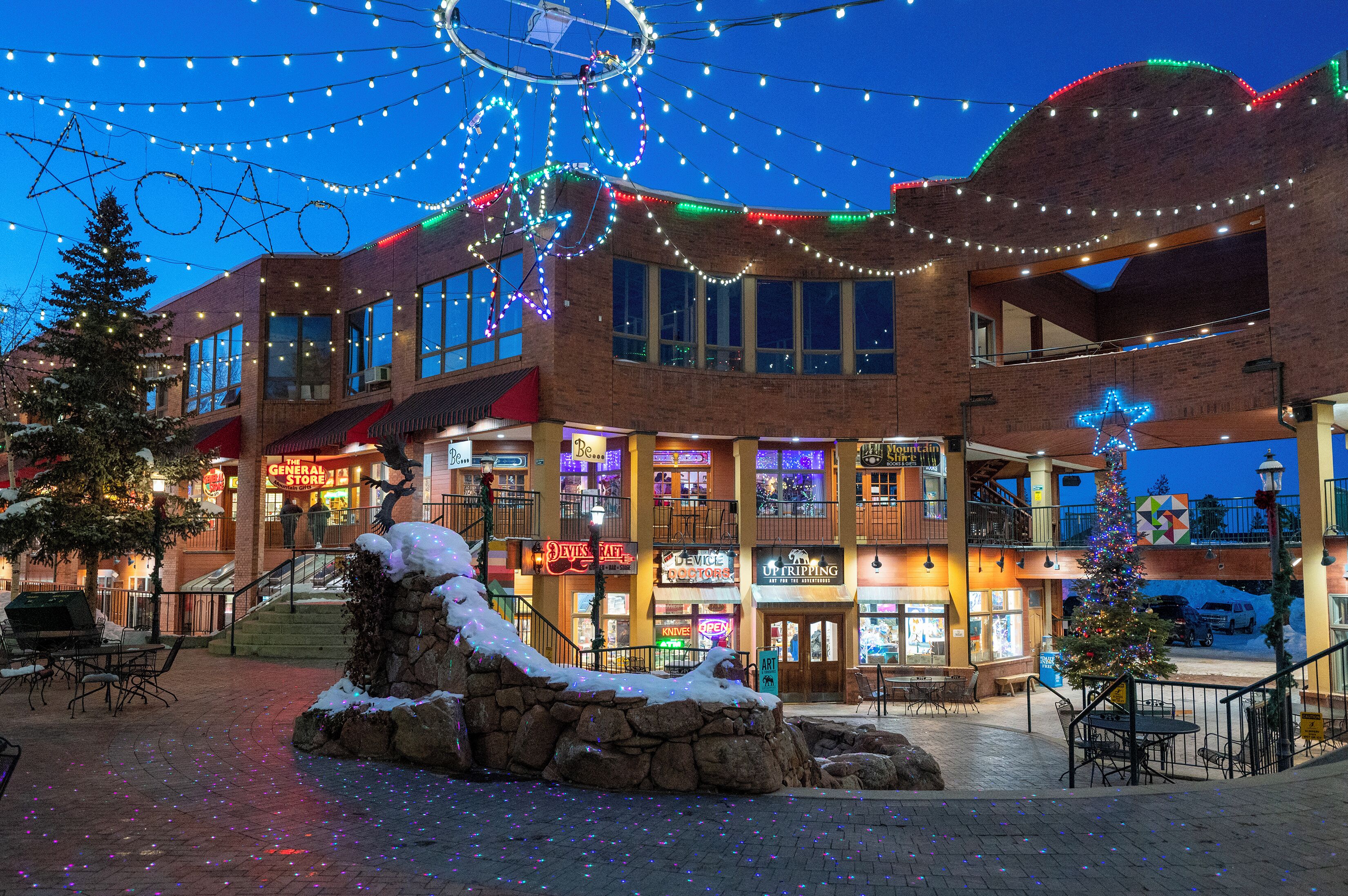 A multi-story building with a brick facade, outdoor seating area, and a Christmas tree.