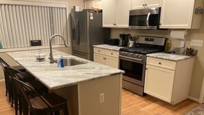 A modern kitchen with a marble countertop, stainless steel appliances, and wooden chairs.