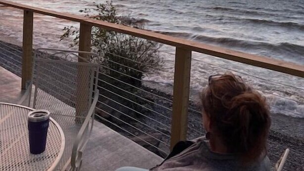 A person seated at a table with a view of the ocean during sunset.