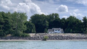 A house with a stone wall and a small tree in front of it, located near a body of water.