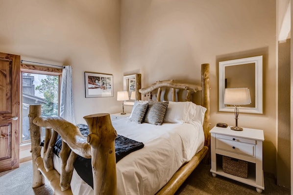 A bedroom with a large bed, wooden headboard, bedside tables, and a window.