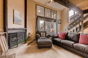 A cozy living room with a fireplace, leather sofas, and a large window.