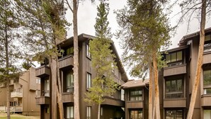 A modern multi-story building with balconies, large windows, and a grassy courtyard with a picnic table. - Perfect Ski In/Ski Out Condo in Center Village (Copper Mountain)