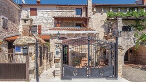 A stone building with a gated entrance, a balcony with a tiled roof, and a sign indicating it is an apartment.