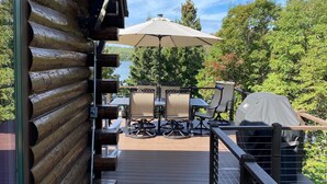 A wooden deck with outdoor furniture, including chairs and a table, and a covered grill area. - Spacious cabin on beautiful Caribou Lake (Lutsen)