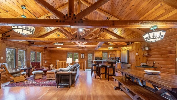 A log cabin interior with a wooden dining table, benches, a fireplace, and a kitchen area. - Spacious cabin on beautiful Caribou Lake (Lutsen)