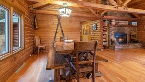 A log cabin interior with a wooden dining table, chairs, a fireplace, and a bookshelf. - Spacious cabin on beautiful Caribou Lake (Lutsen)