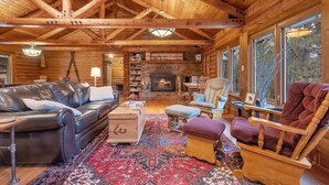 A log cabin interior with a fireplace, leather sofa, wooden rocking chair, and a patterned rug. - Spacious cabin on beautiful Caribou Lake (Lutsen)