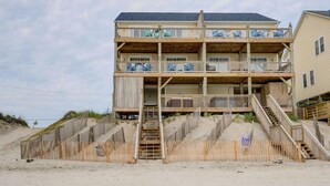 Et flerlags sommerhus ved stranden med træbalkoner og en trappe til indgangen.