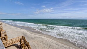 En strand med træpromenader, der fører ned til vandet, en klar himmel og bølger, der ruller ind mod kysten.