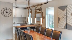 Ein moderner Essbereich mit Holztisch und Ledersesseln, einer großen Wanduhr und einer Küche im Hintergrund.