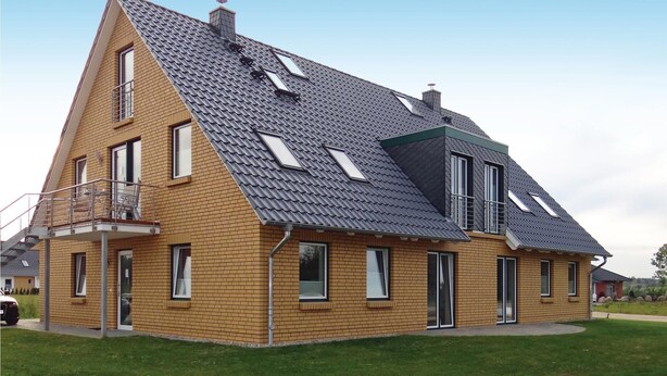 Une maison à deux étages avec un toit en pente, de nombreuses fenêtres de toit et un balcon.