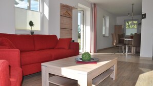 Un salon moderne avec un canapé rouge, une table basse en bois et un coin repas comprenant une table et des chaises.