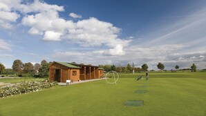 Un bâtiment en bois surmonté d’un toit végétalisé, avec une pelouse bien entretenue et un terrain de golf en arrière-plan.