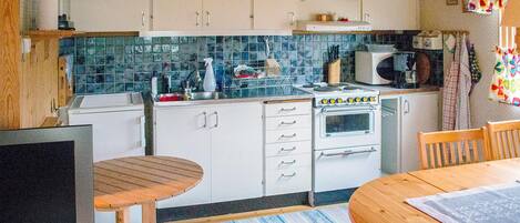 Una cocina con armarios blancos, una estufa, un microondas y una zona de comedor con mesa y sillas.