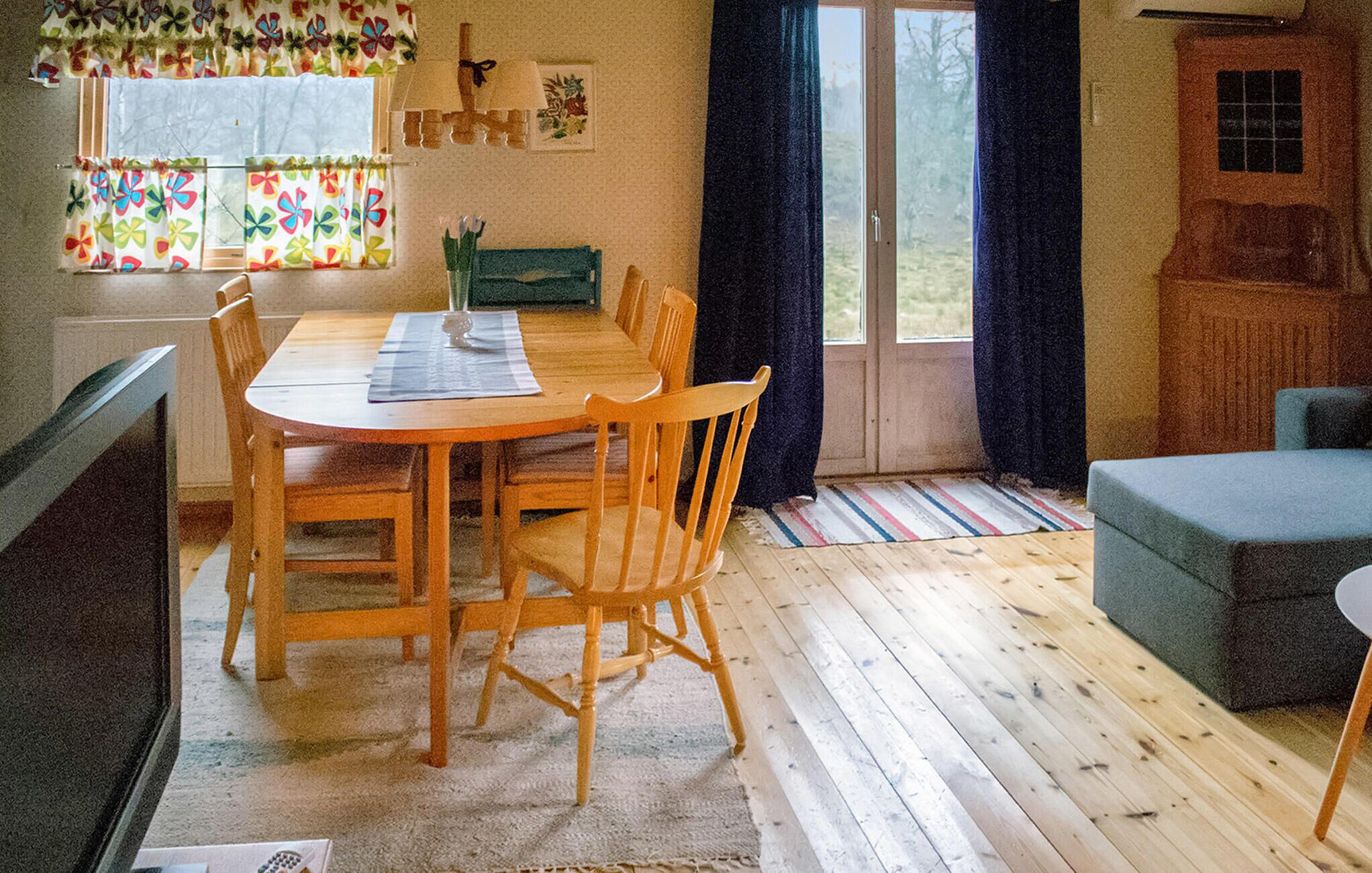 Une pièce chaleureuse avec une table à manger en bois, des chaises, un canapé et une fenêtre avec des rideaux.