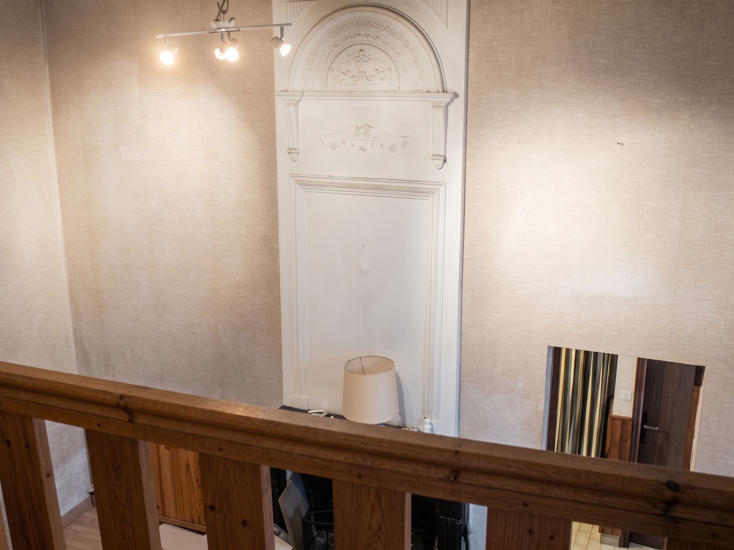 A staircase with a wooden railing, a white door with decorative moldings, and a light fixture above.