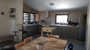 A modern kitchen with a dining area, featuring a central island, built-in appliances, and a large window providing natural light. - Quiet family house (Agde)