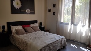 A bedroom with a bed, a nightstand, a lamp, a coffee maker, and a window with curtains. - Quiet family house (Agde)