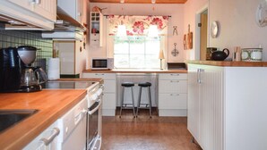 A compact kitchen with a wooden countertop, a microwave, a kettle, and a coffee maker. There are two stools and a window with a floral curtain. - 2 bedroom amazing home in Burseryd (Burseryd)