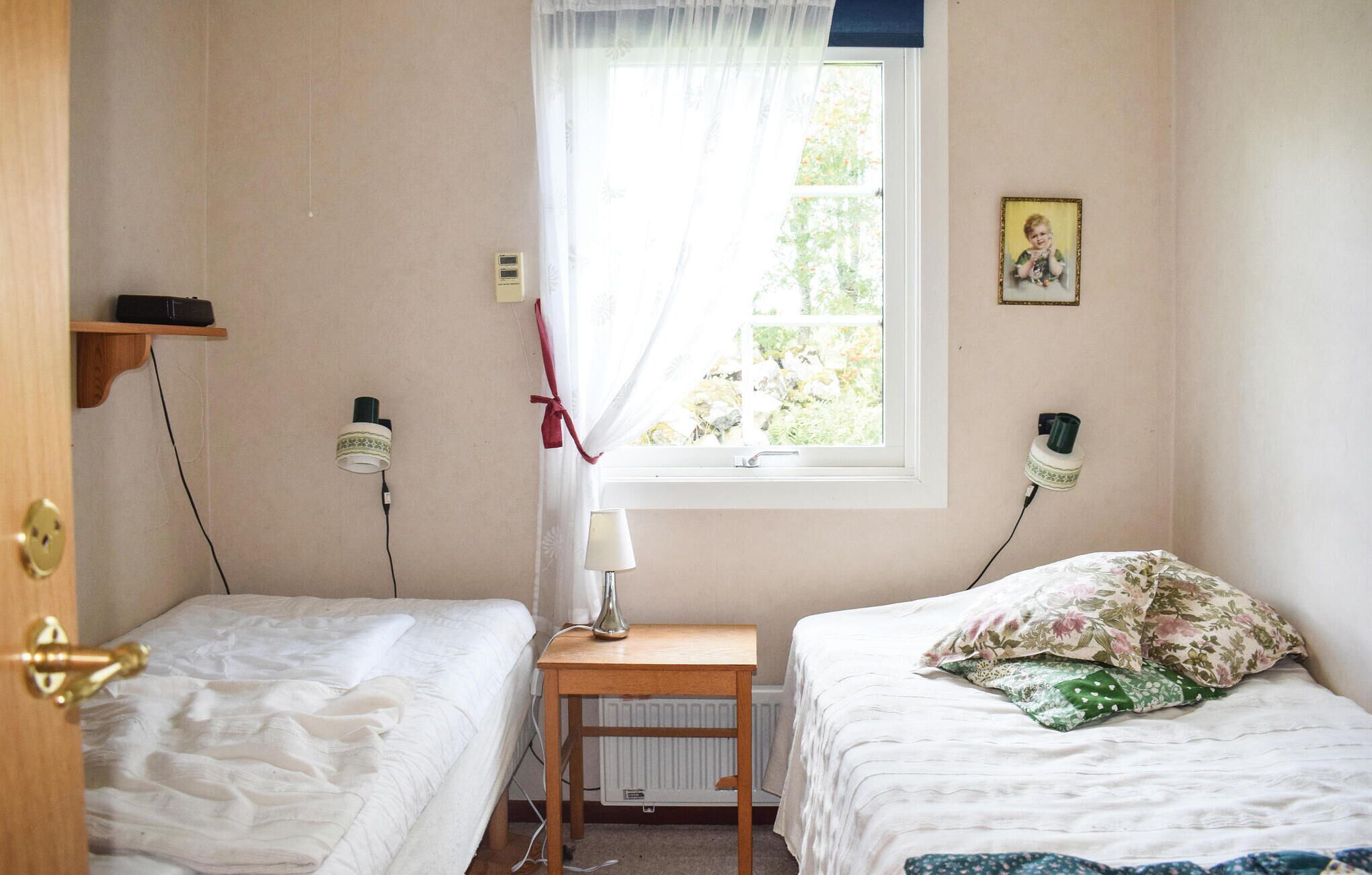 Une chambre avec deux lits, une fenêtre avec des rideaux légers, une table de chevet avec une lampe et un radiateur.