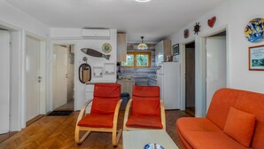 Ein modernes Wohnzimmer mit zwei orangefarbenen Sesseln, einem Sofa und einer Küche im Hintergrund.