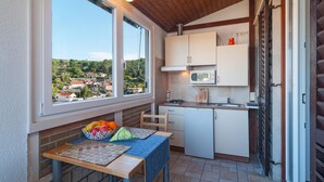 Une cuisine compacte donnant sur un quartier résidentiel, une table à manger avec un panier de fruits et une petite fenêtre.