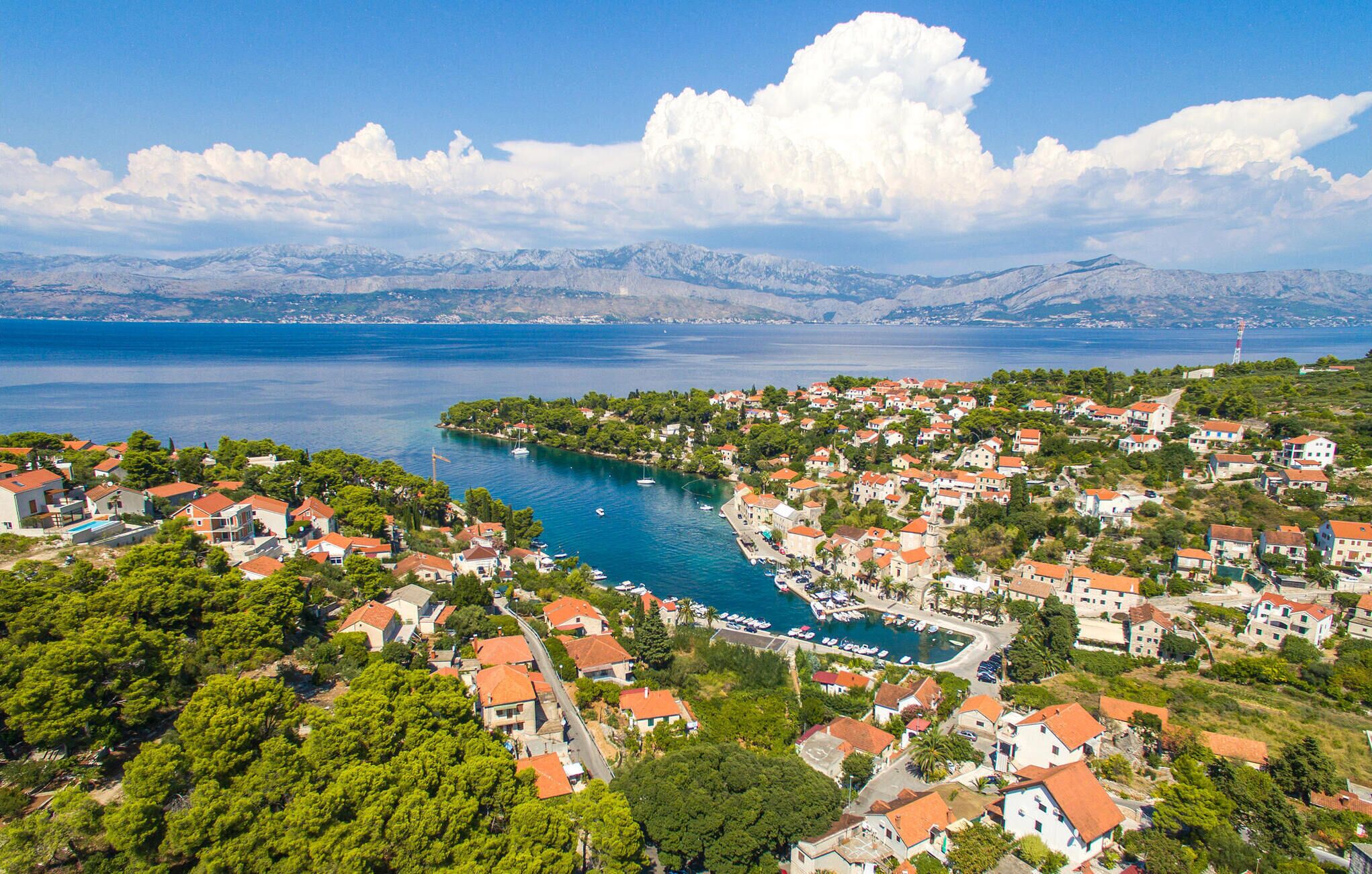 A coastal town with houses, a marina, and mountains in the background.