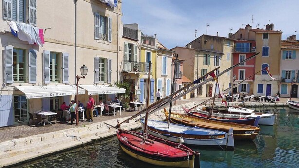 A waterfront scene with boats docked, a restaurant named "Le Mirrot" with outdoor seating, and colorful buildings along the water.