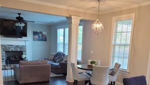A spacious living room with a fireplace, a dining area with a table and chairs, and a kitchen visible in the background. - Spacious Beautiful home for Masters (Evans)