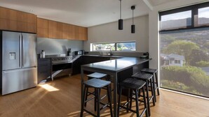 A modern kitchen with a large island, stainless steel appliances, and a view of a residential area.