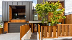 A modern two-story house with a garage, wooden deck, and a tree in the front yard.