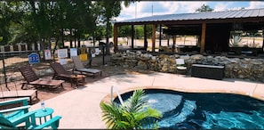 A pool area with lounge chairs, a covered seating area, and a stone wall. - Beautiful Log cabin overlooking a meadow (Pipe Creek)
