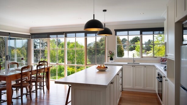 A modern kitchen with large windows, wooden dining table, and pendant lighting.