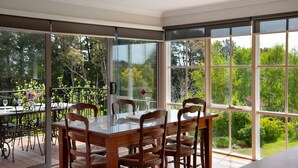 A dining area with a glass table and wooden chairs, overlooking a lush garden.