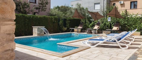 En pool med ett vattenfall, omgiven av solstolar och parasoller.