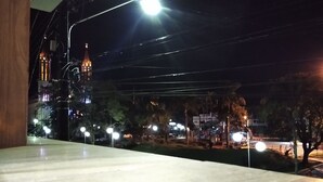 A nighttime view from a window overlooking a street with streetlights and a building with a lit tower. - Pousada Vó Celina (Praia Grande)
